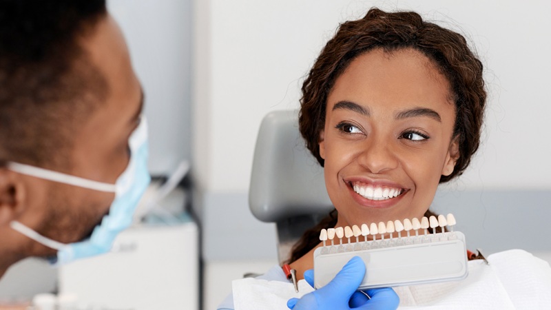 Dentist applying tooth scale samples set to smiling patient with cosmetic veneers